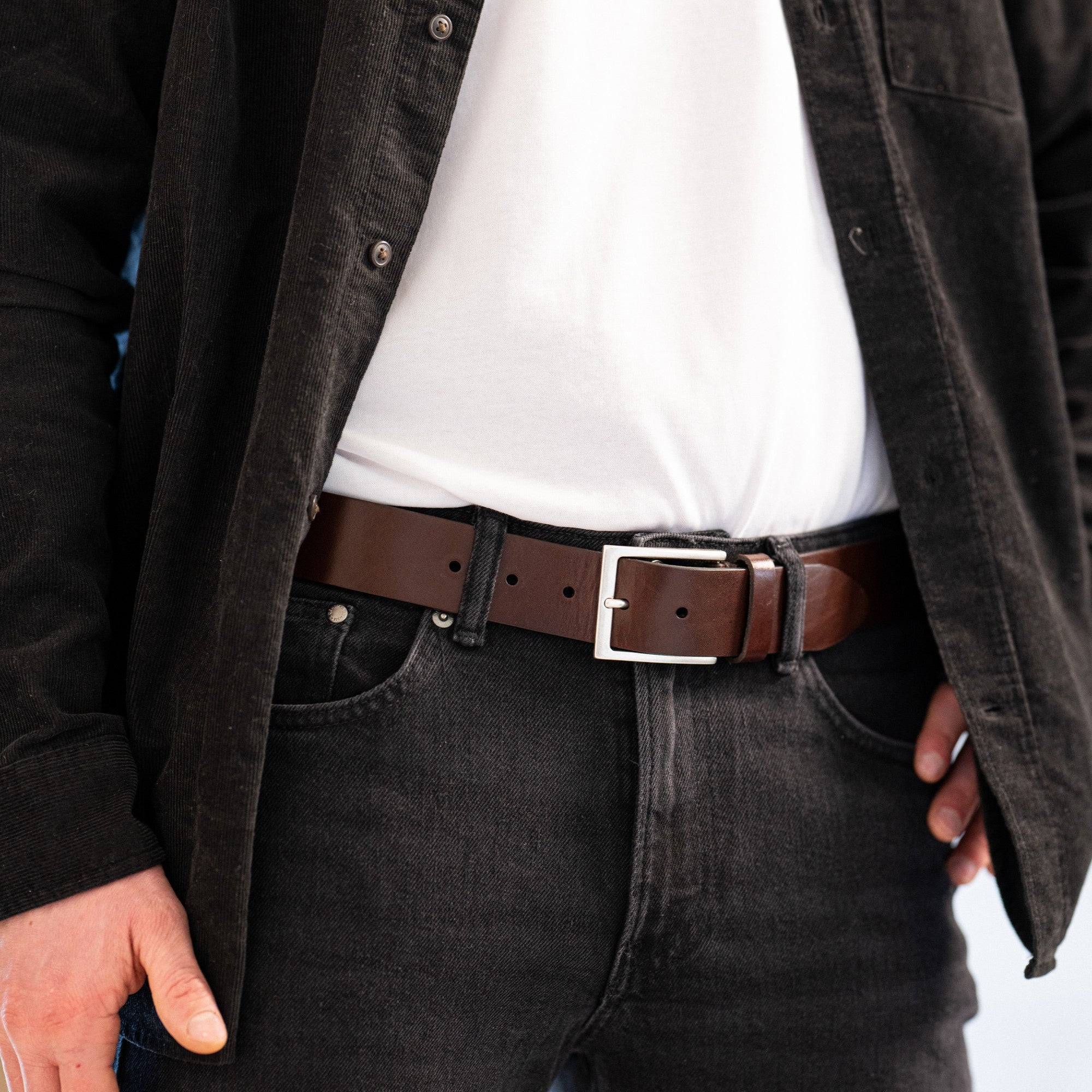 Mann mit dunkler Jeans und schwarzem Cordhemd, dazu ein breiter Jeans Ledergürtel in dunkelbraun