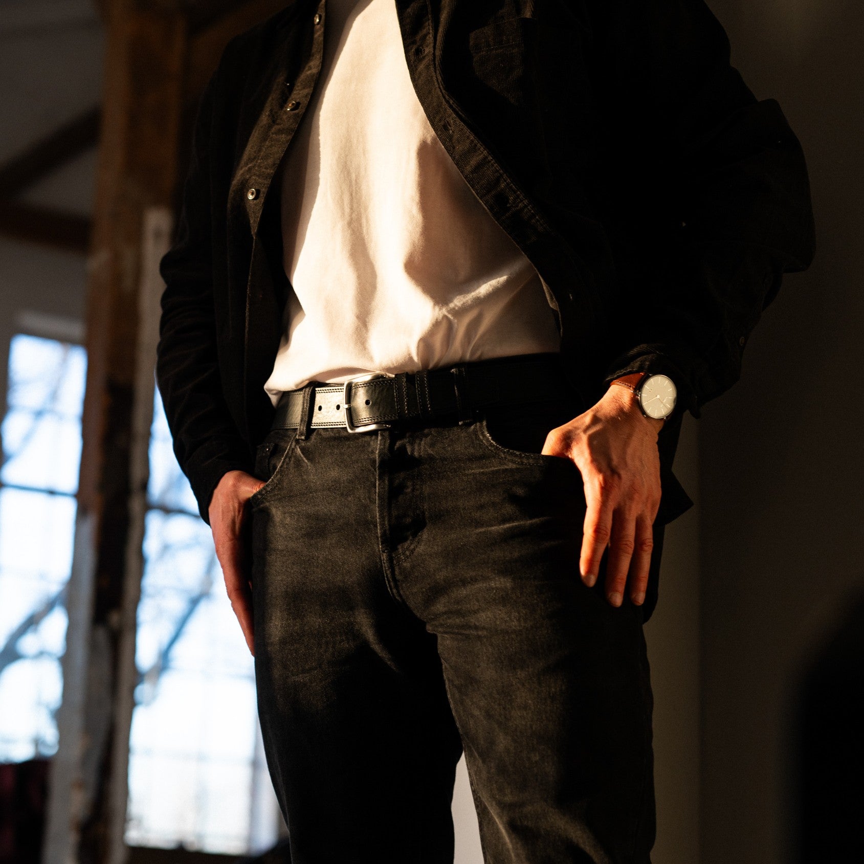 Mann mit schwarzer Jeans und schwarzem Hemd, kombiniert mit einem Jeansgürtel in schwarz, zweifach abgesteppt