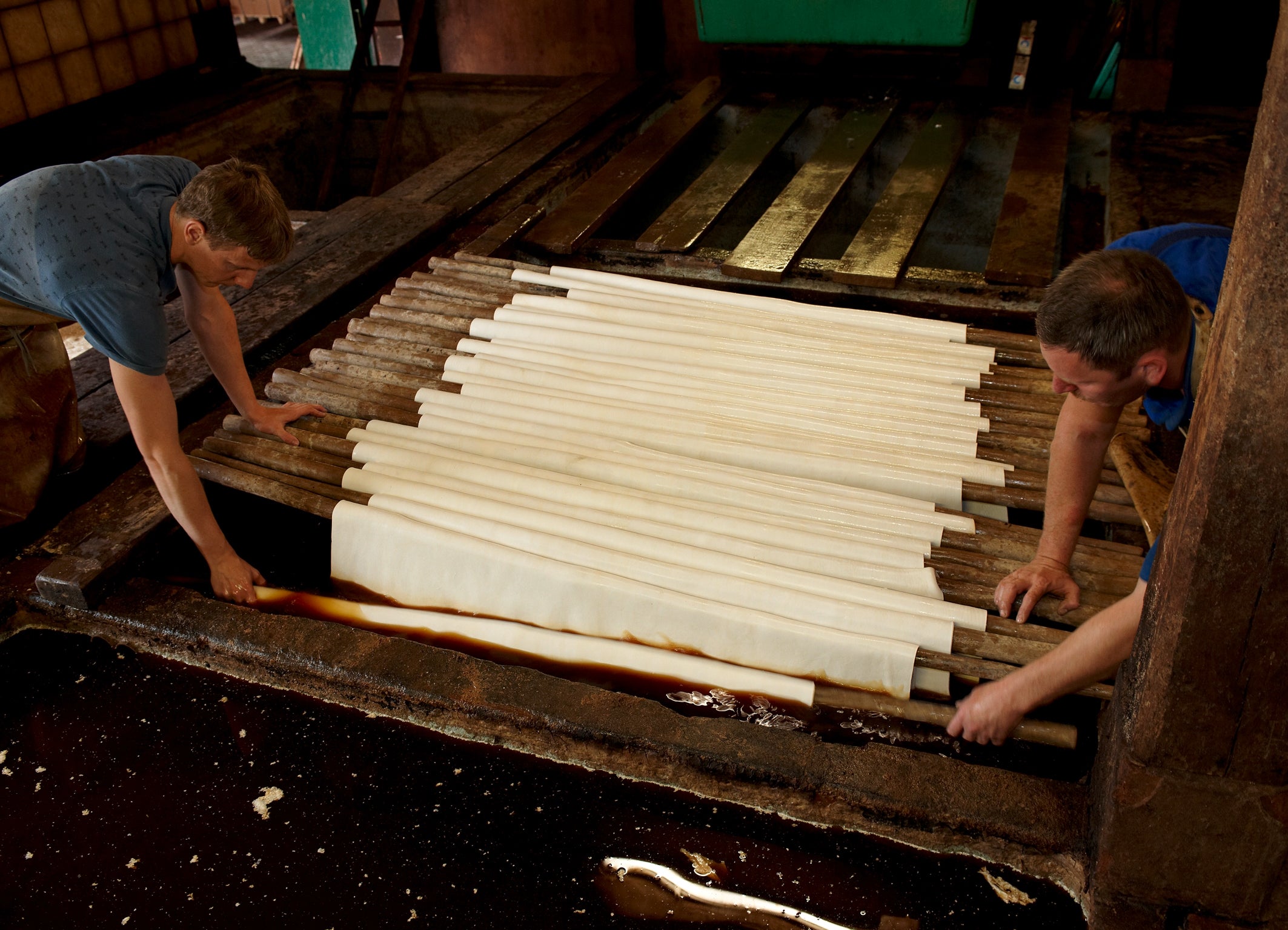zwei Männer hängen schwere Lederhäute in die Gerbgrube