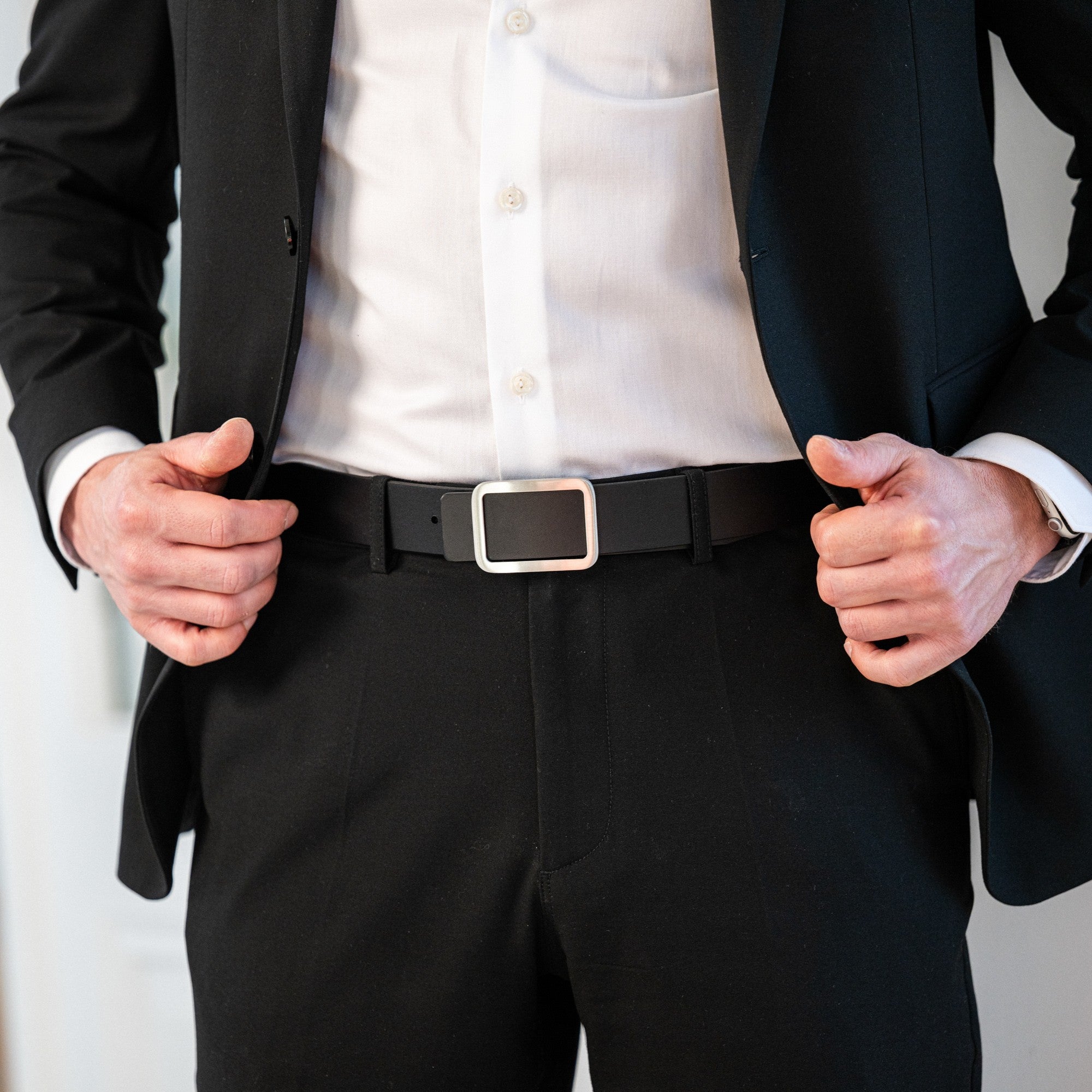 Mann in schwarzem Anzug mit weißem Hemd, kombiniert mit einem minimalistischem Ledergürtel ins schwarz mit silberner Schnalle